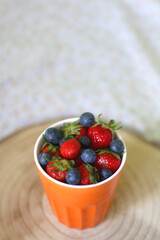 Cup of blueberries and strawberries on a bed. Selective focus.