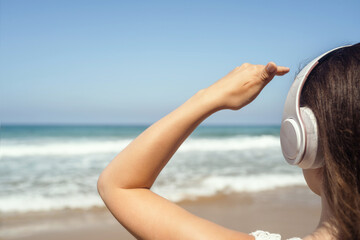 Alone woman on a beach in headphones listen music looking on the sea. Female relaxation at summer vacation. Back view