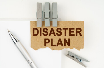 On a white background lies a notebook, a pen, clothespins and cardboard with the inscription - Disaster Plan