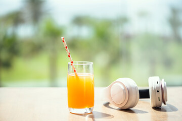 Headphones, orange juice on the table in the palm tree forest. Summer vocation. Copy space. Concept