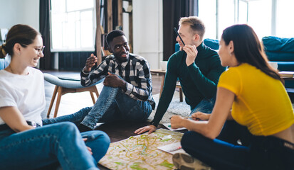 Naklejka premium Positive multiethnic colleagues talking to each other sitting on floor in modern office