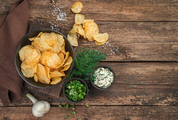Potato chips, fresh herbs and sauce on a wooden background.