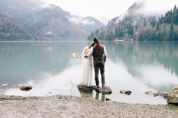 The concept of a wedding. A happy married couple in love in wedding clothes hugs stands in the middle of a boat pier a lake and misty mountains in nature in a fabulous place outdoors