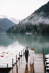 The concept of a wedding. A happy married couple in love in wedding clothes hugs stands in the middle of a boat pier a lake and misty mountains in nature in a fabulous place outdoors