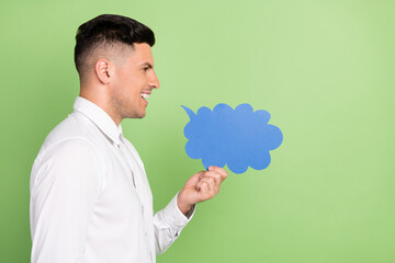 Photo of pretty funky young guy dressed white shirt holding speaking bubble empty space isolated green color background