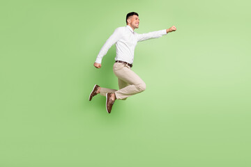 Full length photo of cute funny gentleman wear white shirt smiling jumping high looking empty space isolated green color background