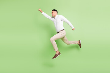 Full length photo of sweet attractive young guy dressed white shirt running fast jumping empty space isolated green color background