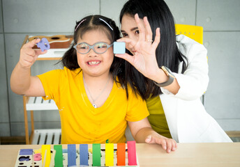 Spacial classroom of disabled kids or autism child learning and painting at a paper with teacher helping in the classroom..