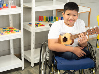 Portrait of disabled child in a wheelchair is playing the ukulele in sensory activity. Concept disabled child learning in school.