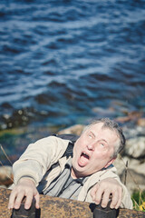 Freak clings his hands to the edge of the cliff above the water