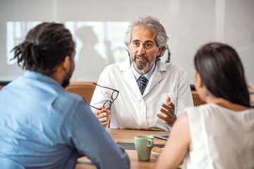 Obraz premium Senior healthcare worker discussing with couple. Male doctor is showing digital tablet to man and woman. They are sitting in hospital. Consultation In Doctors Office