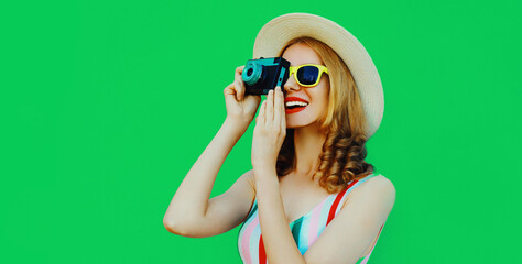 Summer portrait of happy smiling young woman with retro camera wearing a straw hat on green background