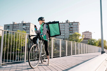 Delivery woman sitting on bike and using smartphone