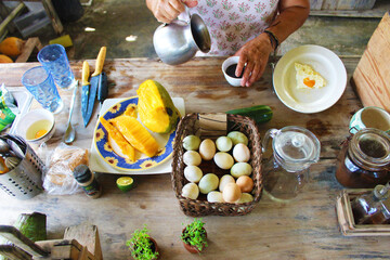 Woman preparing breakfast using fresh eggs, papaya, coffee at the countryside on the wooden counter