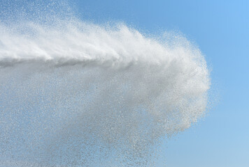 Powerful jet of water from the fire hose of the car against the background of the blue sky