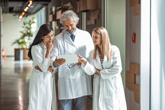 In the Hospital Doctors have Discussion while Using Tablet Computer. In the Background Patients and Medical Personnel. New Modern Fully Functional Medical Facility.