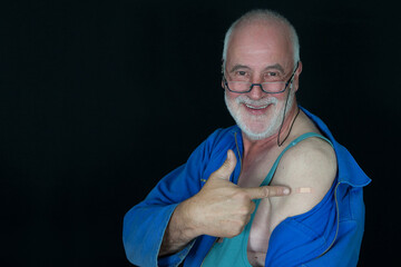 Older craftsman is happy about his second corona vaccination and shows smiling at the band aid on...
