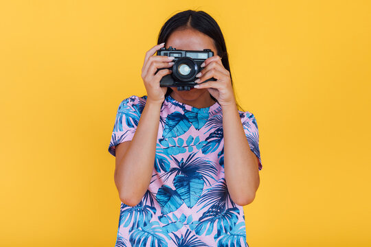 Unrecognizable woman taking photo on camera on yellow background