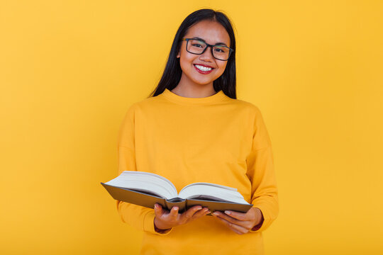 Smart ethnic student reading book on yellow background