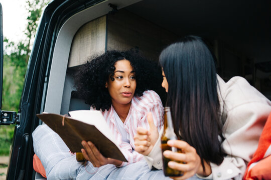 Happy diverse girlfriends with beer reading map in camper van