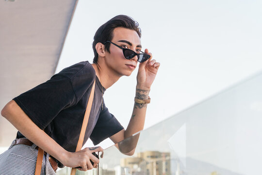 Stylish homosexual man in glasses standing on terrace in city