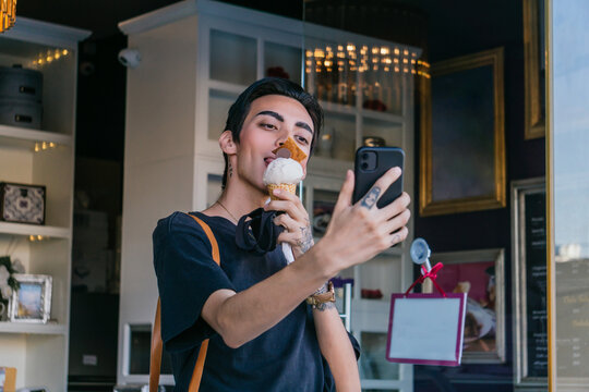 Homosexual man eating ice cream and taking selfie on smartphone