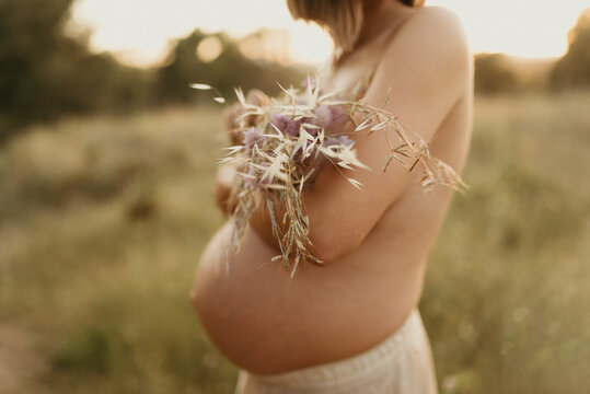 Anonymous topless serene pregnant woman covering breast with flowers in field