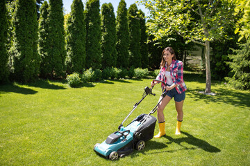 Young woman cutting grass using lawn mower in garden.