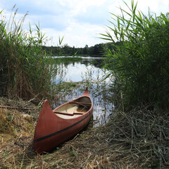 A row boat sitting at the edge of a pond.