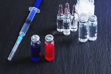 Ampoules with red and blue serum stand on a black background with a syringe and other ampoules