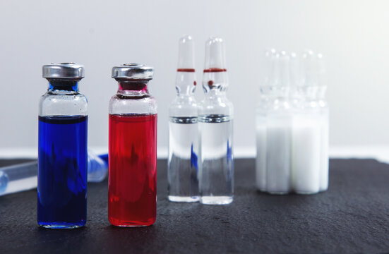 Ampoules with red and blue serum stand against the background of other ampoules. The concept of vaccination
