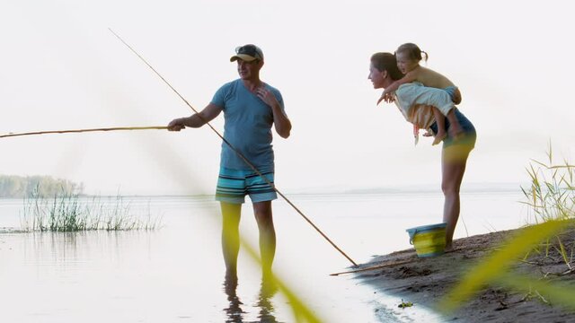 Family fishing on the calm river with retro bamboo fishing rods. Father is fishing, mother and kid have fun around