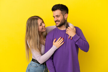 Young couple over isolated yellow background laughing and hugging
