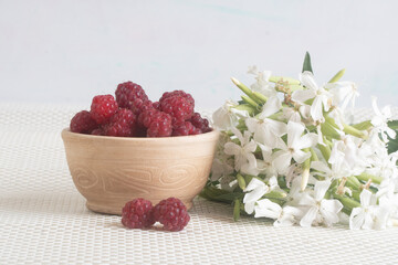 raspberries and flowers. ripe berries on a white tablecloth. summer harvest
