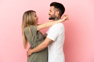 Pregnant woman and man over isolated pink background hugging