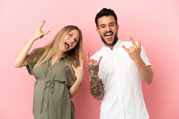 Pregnant woman and man over isolated pink background making rock gesture