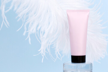 Pink squeeze bottle cream tube with black screw cap and large white ostrich feather on blue background. Moisturizing soft cosmetics concept, mockup. Natural organic spa cosmetics, mockup.