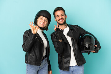 Couple with motorcycle helmet over isolated blue background showing an ok sign with fingers