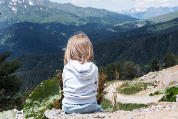 Naklejka premium The child is sitting and looking at the landscape of the Caucasus Mountains. Outdoor travel, local travel.