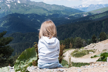 The child is sitting and looking at the landscape of the Caucasus Mountains. Outdoor travel, local travel.