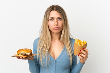 Young blonde woman holding fried chips and cheeseburger over isolated background