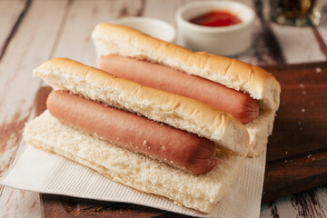 Very high view of a pair of hotdogs without garnishes with pots of mustard and ketchup on a rustic wooden tray. Horizontal view. Fast and junk food concept.