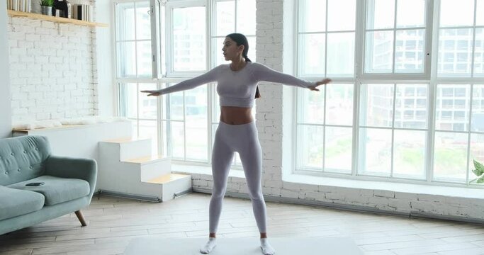 Athletic young woman doing the warm-up before the workout mat at home with large windows in morning. Getting in shape and fit, sport at home during coronavirus pandemic