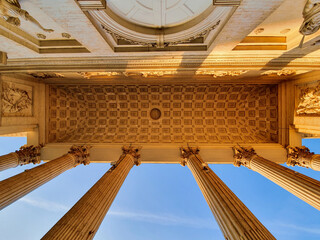 Looking up shot of an old famous building in Brussels, Belgium. Tall sand colored pillars can be seen against a bright blue summer sky. Warm sunlight is passing through reflecting against the entrance