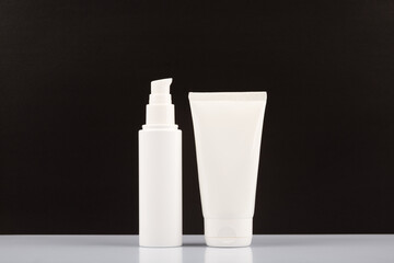 Set of white unbranded cosmetic bottles for daily skincare on white table against black background. Tubes with after shave lotion, face cream or balm on black background. Concept of skin care products
