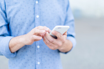 A man in a shirt uses a smartphone in the summer in the city