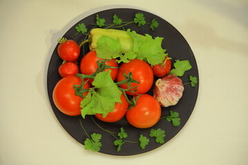 Beautiful red tomatoes on a branch, mushrooms, bell peppers, radishes. parsley. Lettuce. lie down on a black plate. Various fresh raw vegetables. Wonderful. on an isolated white background