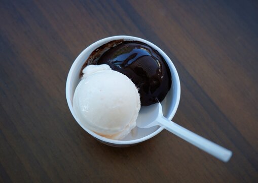 light and dark ice cream scoops in paper cup with white plastic spoon on brown wooden table