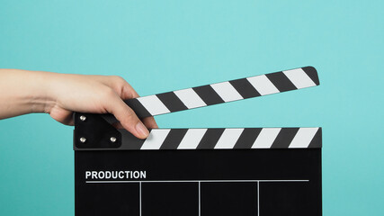 Hand is holding Black clapper board or movie slate on green or mint or Tiffany Blue background.