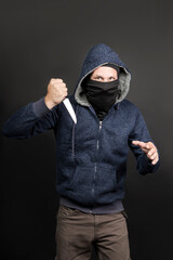 Naklejka na ściany i meble American hooded man with black mask holding knife and looking at the camera. Robbery, violence and economic crisis concept. Caucasian maniac, thief, gangster and a rapist attack with knife. Copy space